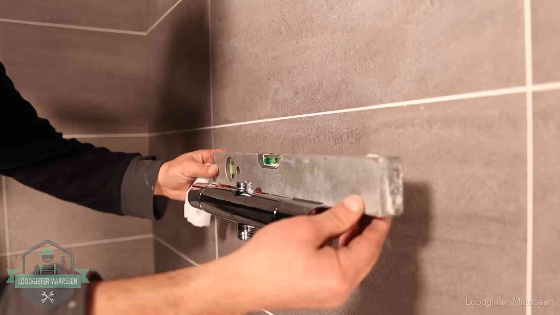 Loodgieter lijnt een douchekraan uit met een waterpas in een woning in Maarssen