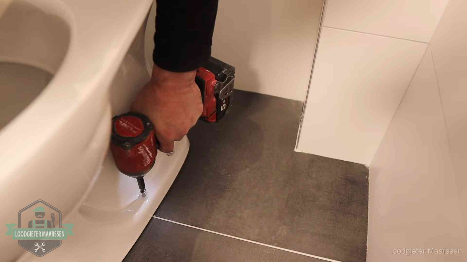 Loodgieter zet de voet van een wc-pot vast op de tegelvloer in Maarssen